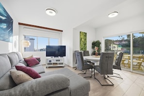 A modern living room with a grey sofa, a flat-screen TV, and a dining area with chairs and a table. - Little Paradise - Funchal (Funchal)