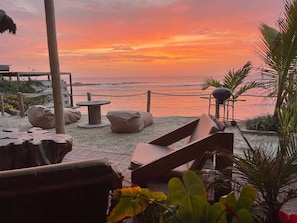 A beachside seating area with a view of the ocean at sunset.