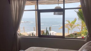 Un dormitorio con un ventanal grande, una cama con colcha estampada y vistas a la playa y al océano.