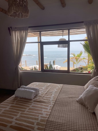A bedroom with a large window overlooking the beach, a bed with a patterned bedspread, and a hanging light fixture.. w Beachview 4BR w Terrace in La Libertad