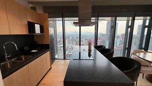 Eine moderne Küche mit einer großen Kochinsel, einer integrierten Spüle und Blick auf eine Stadtlandschaft durch große Fenster.