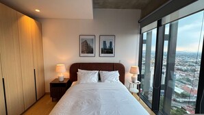 Ein modernes Hotelzimmer mit einem großen Bett, zwei Nachttischlampen, einem Holzschrank und Blick auf die Stadt.