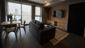 A modern living room with a sofa, a coffee table, a TV mounted on the wall, and a dining area with a table and chairs. - w Calm Cozy 1BR w Balcony in Tabacalera (Mexico City)