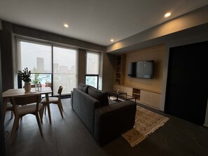 A modern living room with a sofa, a coffee table, a TV mounted on the wall, and a dining area with a table and chairs. - w Calm Cozy 1BR w Balcony in Tabacalera (Mexico City)