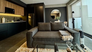 A modern living room with a sofa, a glass coffee table, and a kitchen area with a microwave and refrigerator. - w Calm Cozy 1BR w Balcony in Tabacalera (Mexico City)