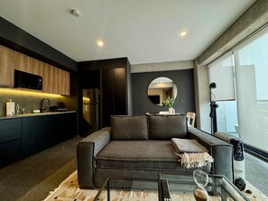 A modern living room with a sofa, a glass coffee table, and a kitchen area with a microwave and refrigerator. - w Calm Cozy 1BR w Balcony in Tabacalera (Mexico City)