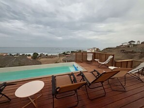 Una terraza de madera con piscina, sillas de descanso y vista al océano.