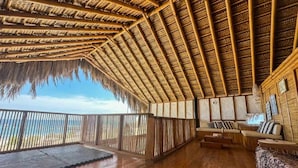 A room with a thatched roof, wooden flooring, a sofa, and a view of the sea. - w Relaxing Oceanfront 5BR in Punta Veleros (Los Organos)