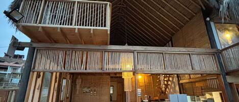 A two-story building with a thatched roof, a balcony with railings, and a dining area with outdoor seating.