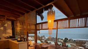 Amplia habitación con un ventanal grande con vistas al mar, zona de comedor de madera y cocina con barra.