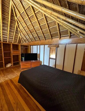 Une piÚce avec un plafond haut, un plancher en bois, un lit, une télévision et des étagÚres intégrées.