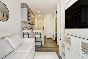 A modern, well-lit room with a white sofa, a small kitchen area with a sink and bar stools, and a large flat-screen TV mounted on the wall. - w Luxury Cozy Loft in Chapinero (Bogotá)