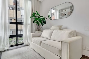 Ein modernes Wohnzimmer mit einem weißen Sofa, einem großen Spiegel und einem Blumentopf.