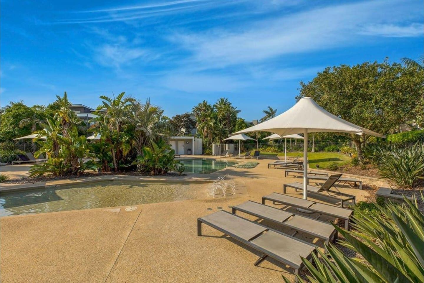 A pool area with lounge chairs and umbrellas, surrounded by tropical plants.