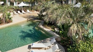 Uma piscina clara com espreguiçadeiras e palmeiras.