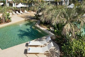 Ein klares Schwimmbecken mit Liegestühlen und Palmen.