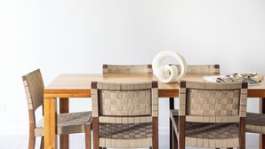 Uma mesa de jantar com quatro cadeiras, um objeto decorativo branco e uma revista sobre a mesa.