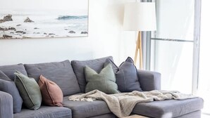 Uma sala de estar moderna com um sofá modular cinza, uma mesa de centro de madeira e uma grande janela com vista para o exterior.