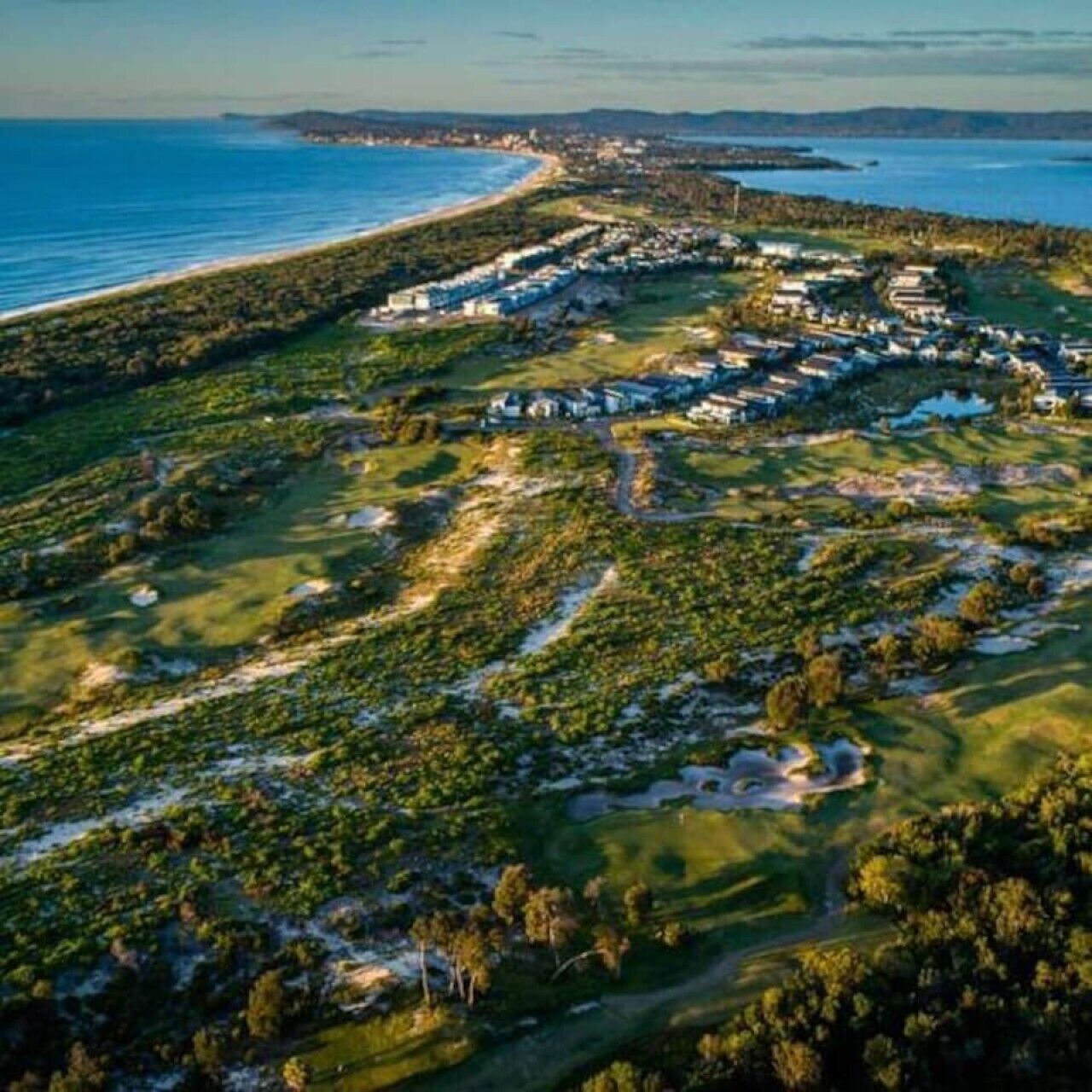 An aerial view of a coastal resort with multiple buildings, green lawns, and a beach.