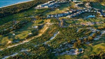 An aerial view of a coastal resort with multiple buildings, green lawns, and a beach.