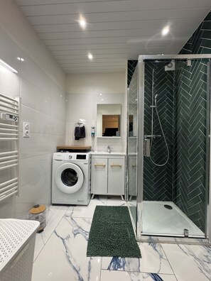 Ein kleines Hotelbad mit Waschmaschine, Waschbecken, Spiegel und Duschkabine.
