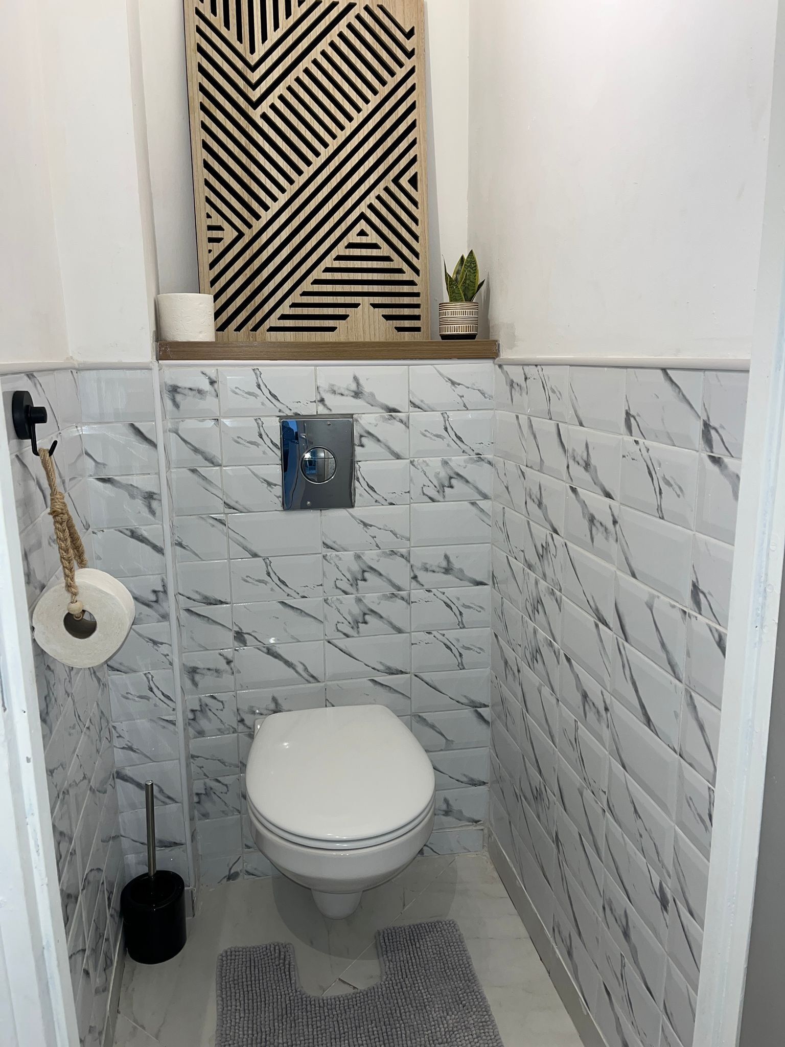 A bathroom with a toilet, a hand dryer, a towel rack, a potted plant, and a decorative panel above the toilet.