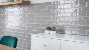 Eine moderne Küche mit grauer Ziegelrückwand, weißen Schränken und einem Holztisch mit Türkisstühlen.