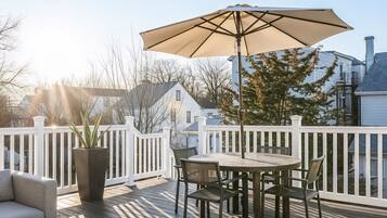 Eine Holzterrasse mit rundem Tisch und Stühlen, einem großen Sonnenschirm und einem Blumentopf.