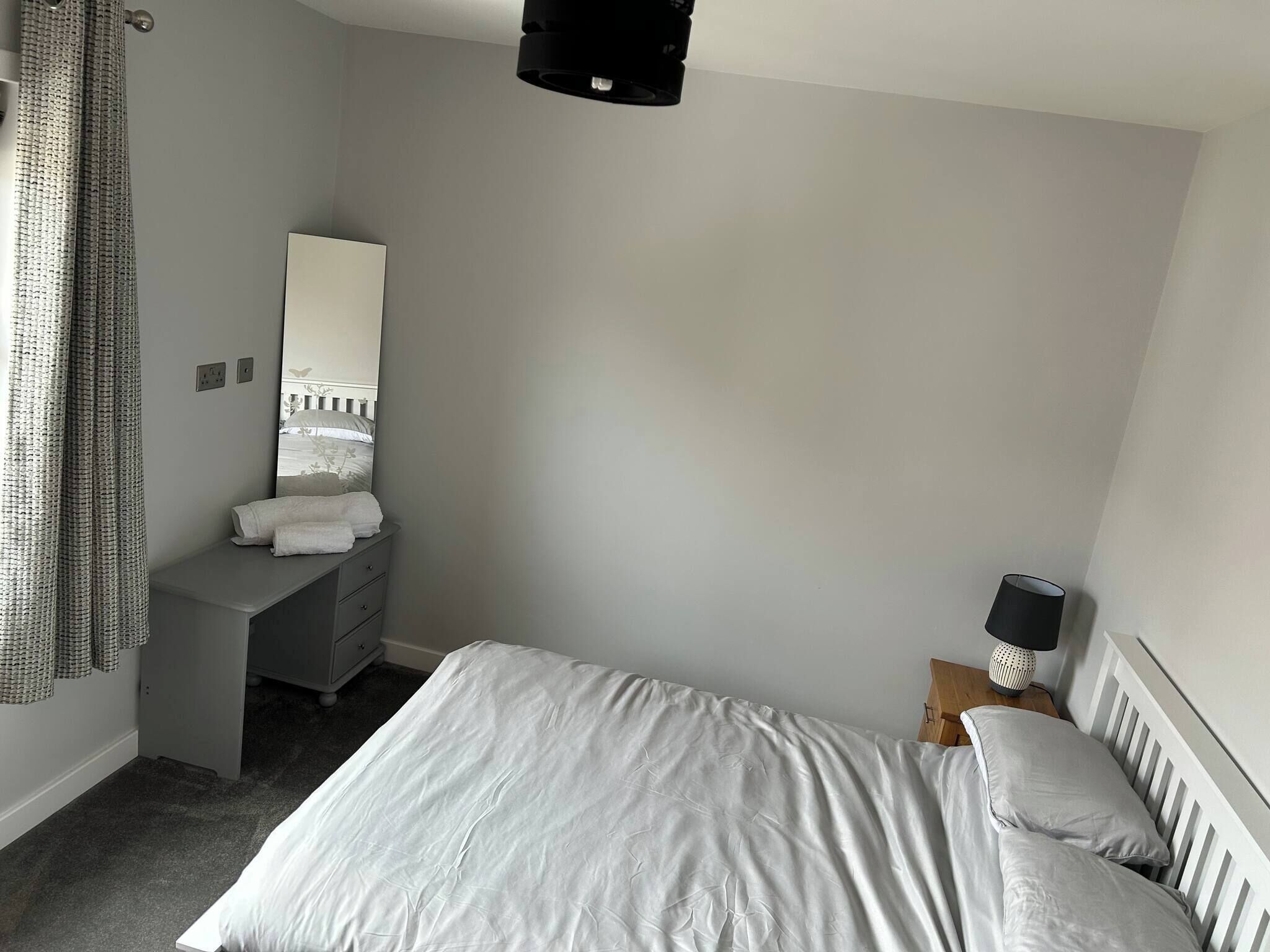 Un dormitorio con cama, cómoda, espejo, lámpara y ventana con cortinas.