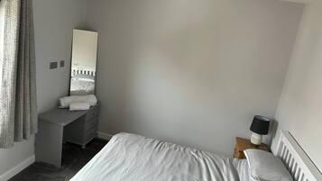Un dormitorio con cama, cómoda, espejo, lámpara y ventana con cortinas.