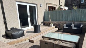 Un patio al aire libre con mobiliario de mimbre, una mesa con superficie de vidrio y una zona de estar cubierta.