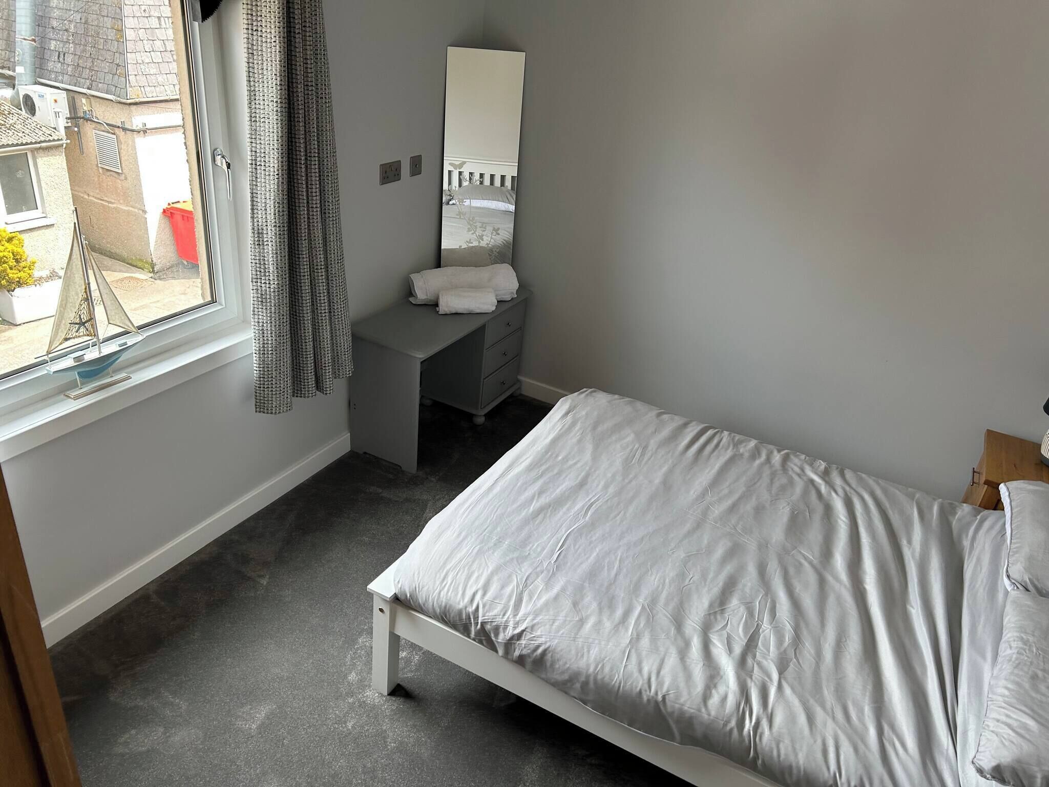 A bedroom with a bed, a dresser, a mirror, and a window with curtains.