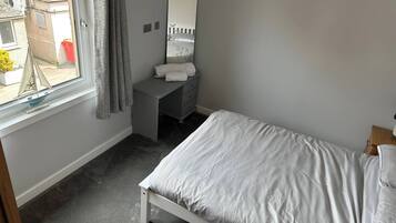 A bedroom with a bed, a dresser, a mirror, and a window with curtains.