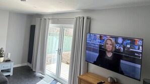 Una sala de estar moderna con televisor, puerta corrediza de vidrio, una mesita y una planta en maceta.