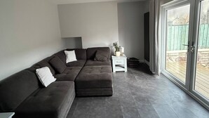 Una sala de estar moderna con un sofá modular, una mesita auxiliar blanca pequeña y un amplio ventanal corredero que da a un espacio exterior.