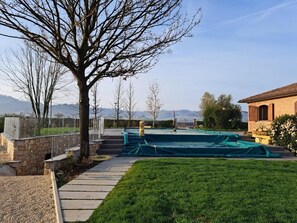 A backyard with a stone wall, a tree, and a green tarp covering an area.