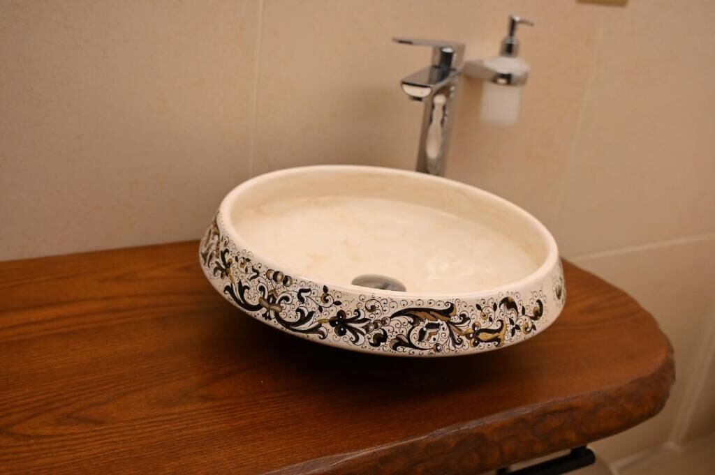 Ett badrum med en vit, keramisk tvättställ med detaljerade, svarta mönster, en träbänkskiva och en modern blandare.