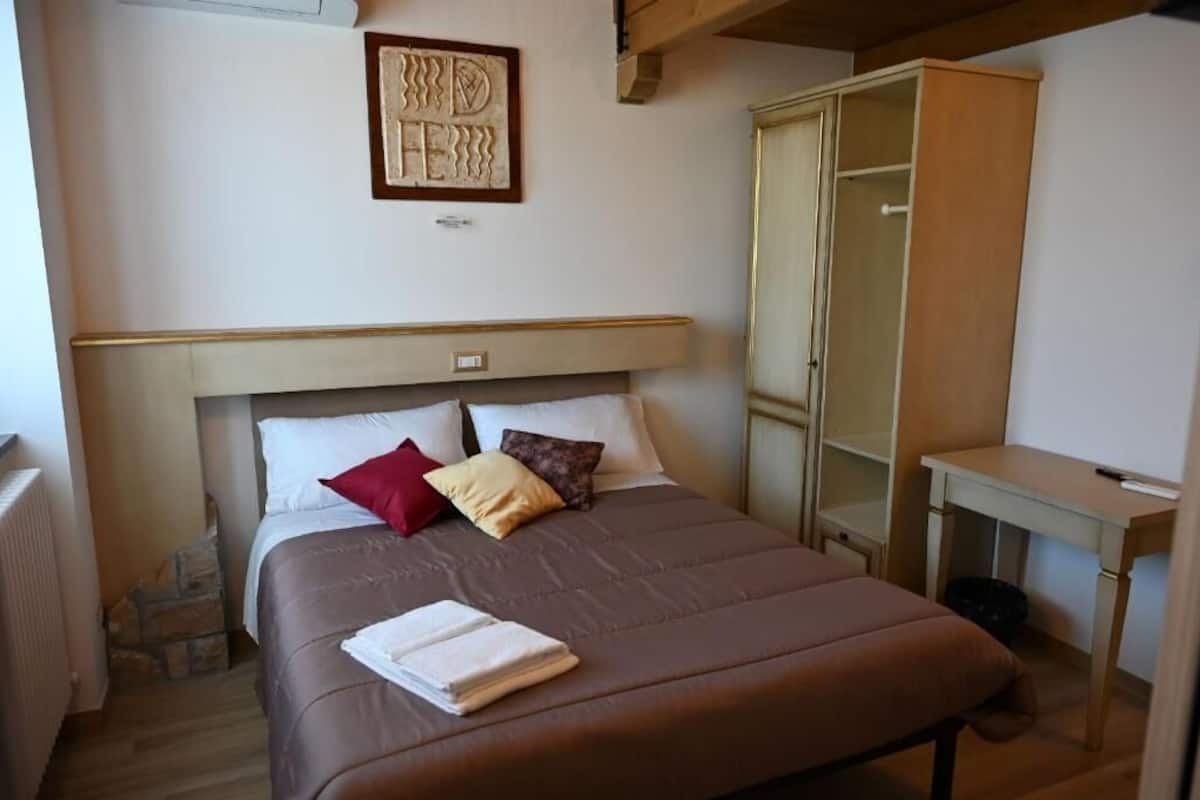 Un dormitorio con cama, armario, escritorio y una obra de arte enmarcada en la pared.