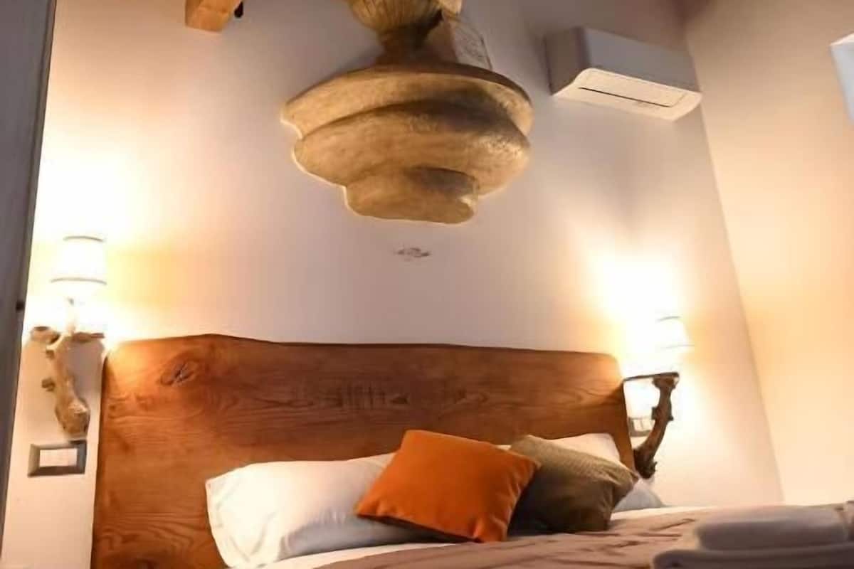 Un dormitorio con techo de madera, una cama con almohadas y una lámpara fijada a la pared.
