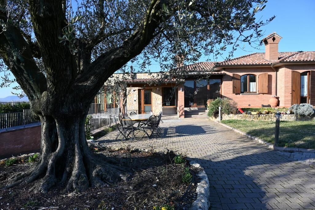 A house with a tiled roof, a large tree in the front yard, and a paved pathway leading to the entrance.