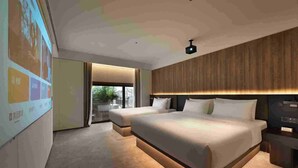 Ein modernes Hotelzimmer mit zwei Betten, einem großen Fenster und einer Projektionsleinwand an der Wand.