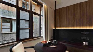 Ein modernes Zimmer mit einem großen Fenster, einem runden Tisch mit einer Obstschale und einer Wandpaneele aus dunklem Holz.