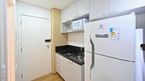 Una cocina compacta con armarios blancos, una encimera negra, un microondas integrado y un refrigerador con panel de control.