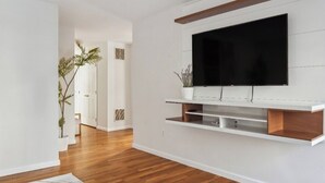 Una sala moderna con un televisor de pantalla plana montado en una pared blanca, piso de madera y un tapete grande de diseño abstracto.