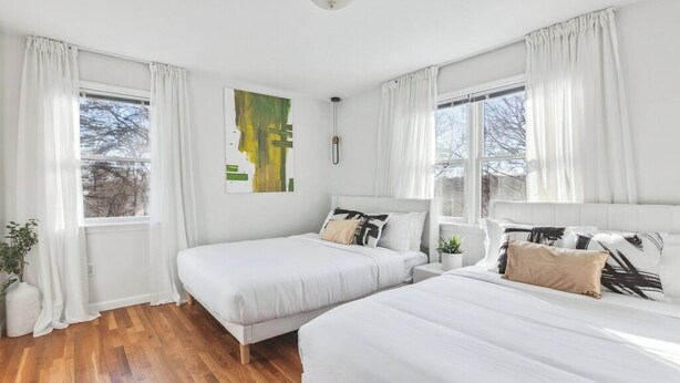 Una habitación con dos camas, cortinas blancas, una lámpara en el techo y una ventana con vistas.