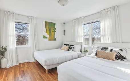 A room with two beds, white curtains, a ceiling light, and a window with a view.