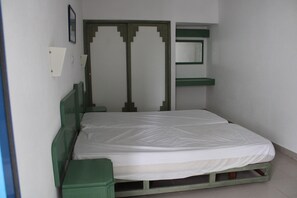 A single bed with a green frame, a white mattress, and a green headboard. There is a small bedside table and a mirror on the wall. - Apartment in Praia da Rocha (Portimão)
