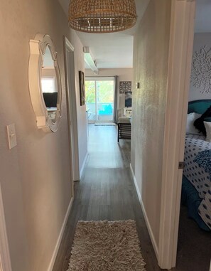Ein Flur mit einem Spiegel, einer gewobenen Leuchte, einem Teppich und einem Bett mit einer gemusterten Tagesdecke.