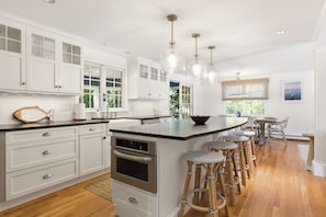 A modern kitchen with white cabinetry, a central island with stools, stainless steel appliances, and pendant lighting. - Gorgeous, Stylish Home - Ping Pong & Firepit (Chatham)