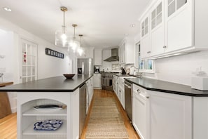 A kitchen with white cabinetry, a black countertop, stainless steel appliances, and a hanging light fixture. - Gorgeous, Stylish Home - Ping Pong & Firepit (Chatham)